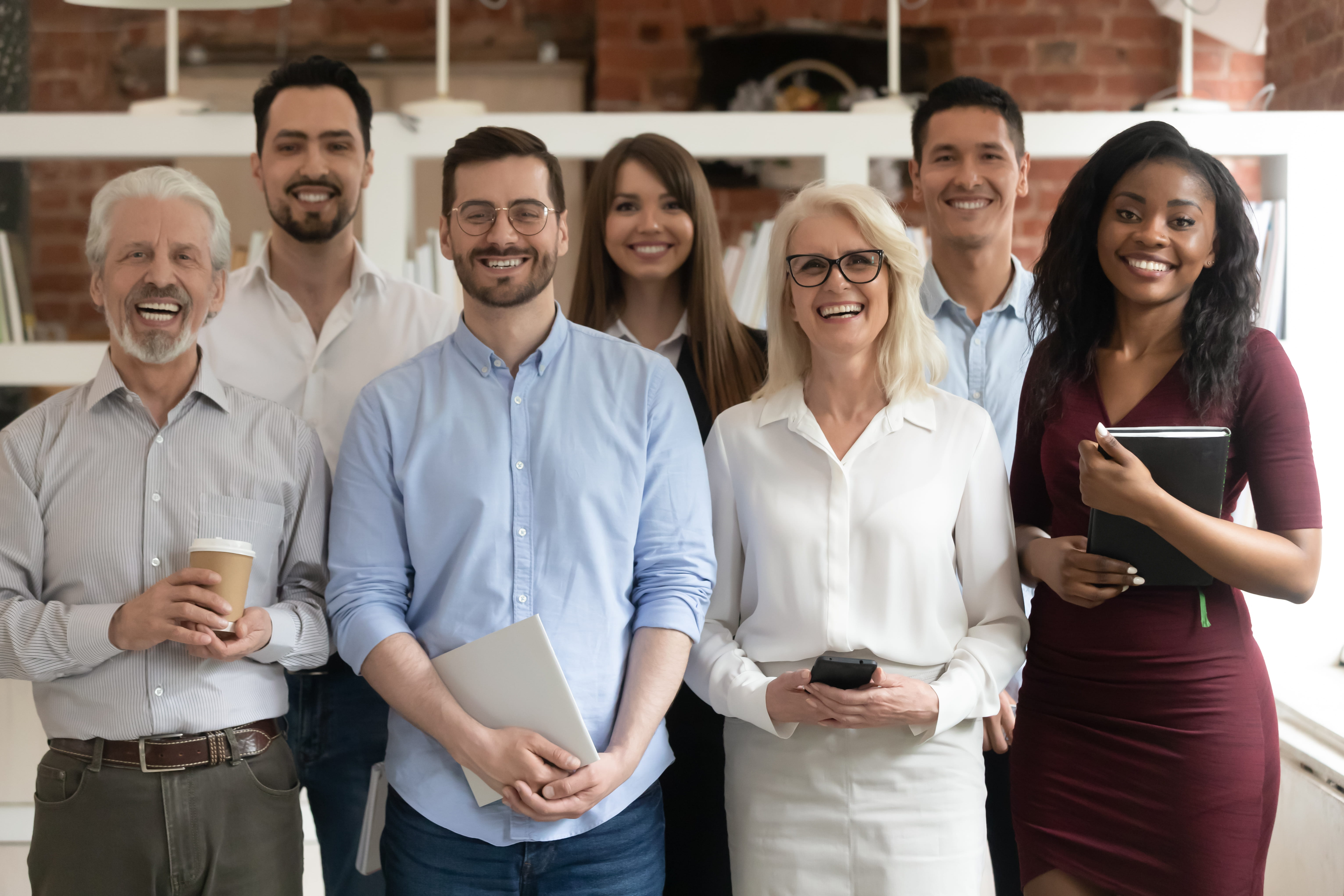 Diverse collection of individuals in business casual outfits standing in an office setting.